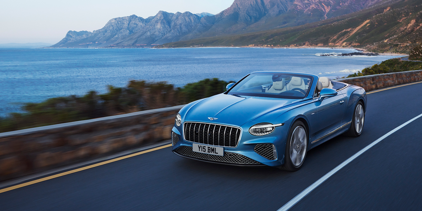 Bentley Maastricht New Bentley Continental GTC Azure convertible in Light Windsor blue paint with 22 inch Azure wheels and chrome grill, driving dynamically by the sea