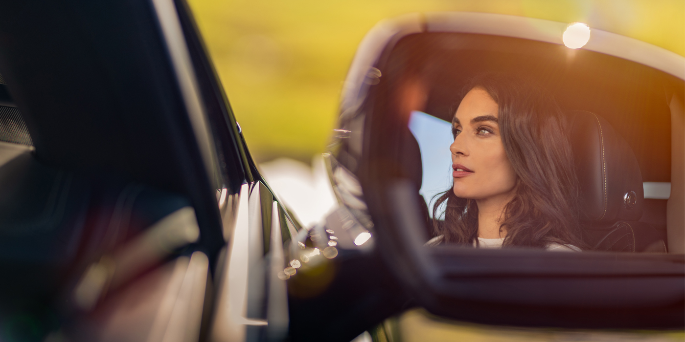 Bentley Maastricht profile of dark haired woman's face in mirror of Bentley car in sunlight