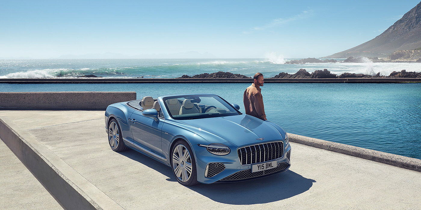Bentley Maastricht New Bentley Continental GTC Azure convertible front view in Light Windsor blue paint with 22 inch ten spoke wheels parked by the sea in the sunshine