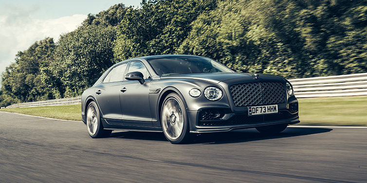 Bentley Maastricht Bentley Flying Spur Mulliner sedan front three quarter in dark grey paint driving dynamically by some trees on a track