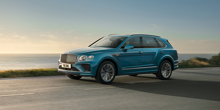 Bentley Maastricht Bentley Bentayga Azure SUV in Topaz blue paint driving dynamically by the ocean with 22 inch 10 spoke directional wheels