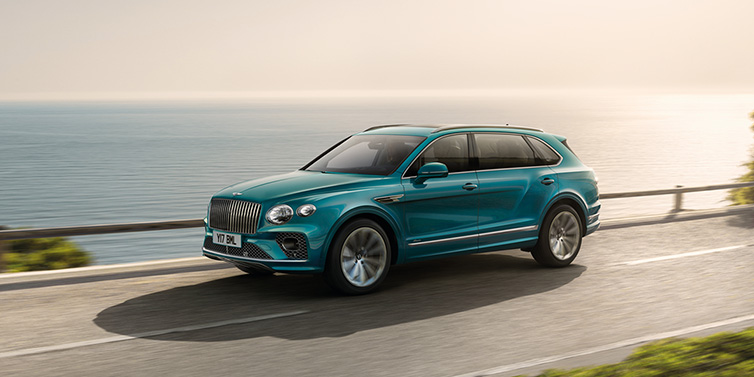 Bentley Maastricht Bentley Bentayga Extended Wheelbase Azure SUV in Topaz blue paint driving dynamically by the ocean