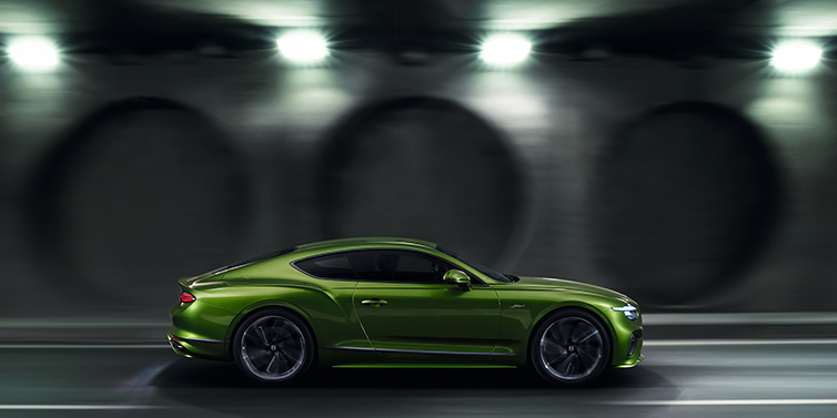 Bentley Maastricht Bentley Continental GT Speed coupe profile in Tourmaline Green driving dynamically past a concrete wall at night