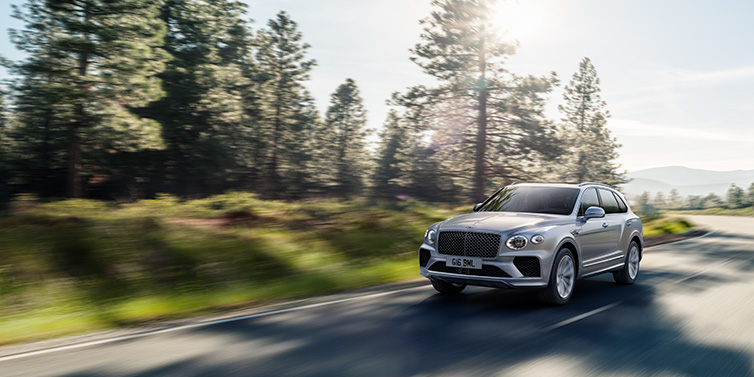 Bentley Maastricht Bentley Bentayga SUV front three quarter in Moonbeam silver paint driving dynamically along a tree-lined road