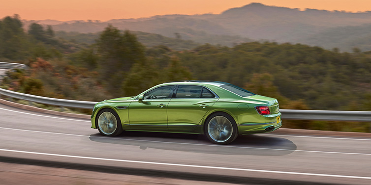 Bentley Maastricht Bentley Flying Spur Speed sedan side profile in Tourmaline Green paint driving dynamically on a mountain road at sunset