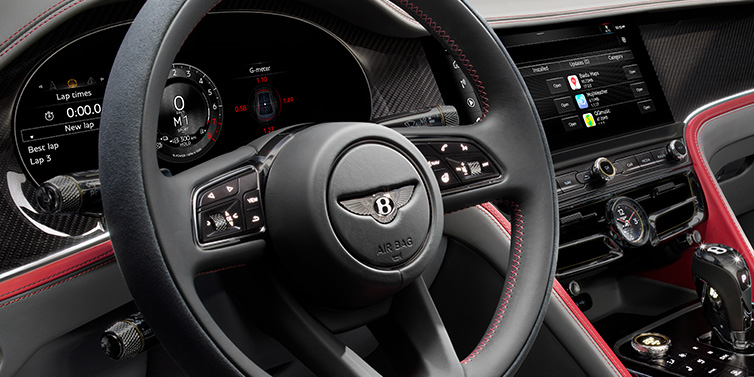 Bentley Maastricht Bentley Flying Spur Speed sedan front interior detail showing steering wheel and driver screens surrounded with Hotspur red and Gravity Grey hides